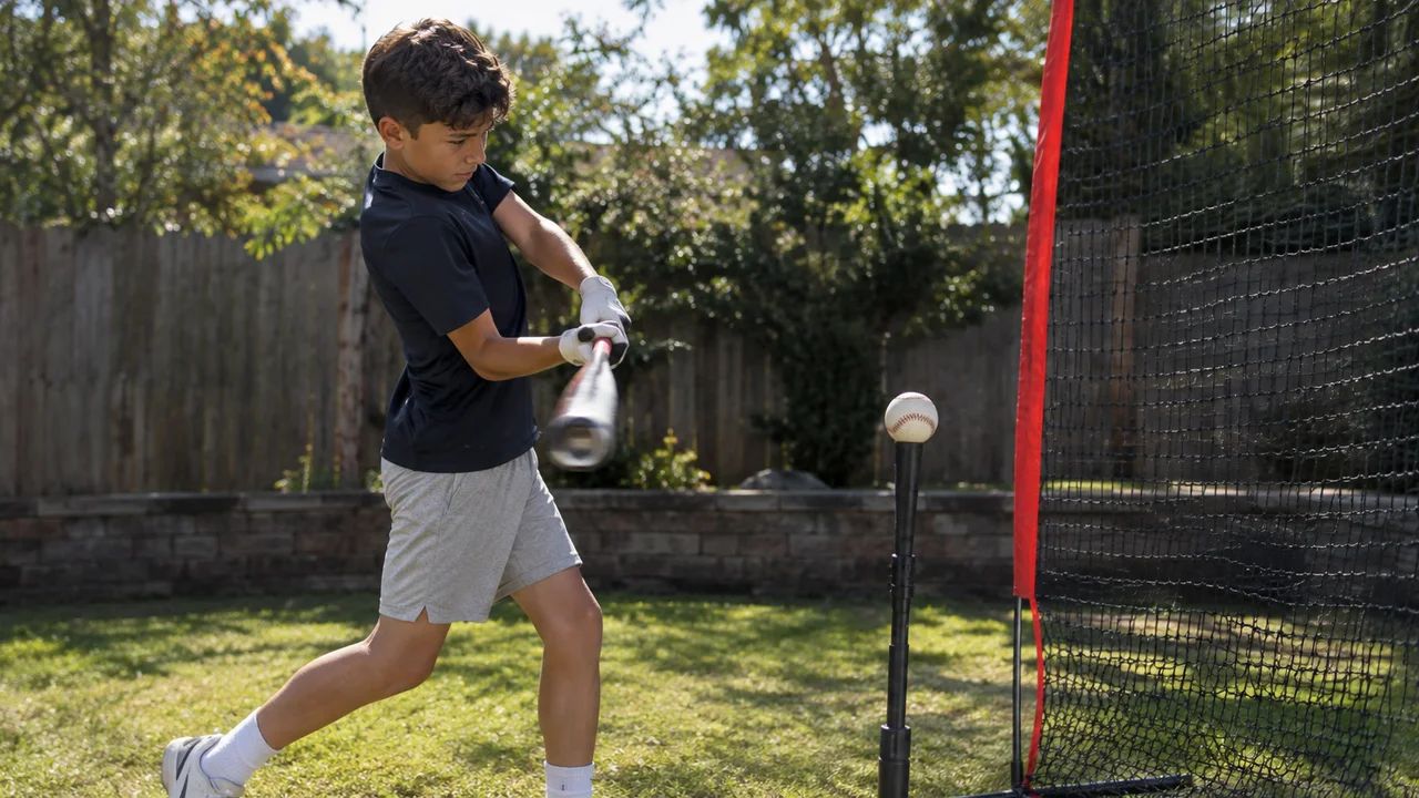 Youth baseball player hitting off a tee into a net in a backyard